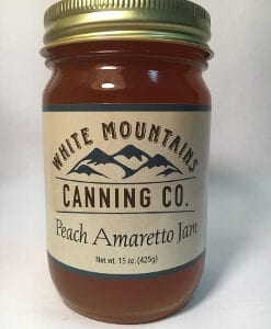 A jar of peach amaretto jam on top of a table.
