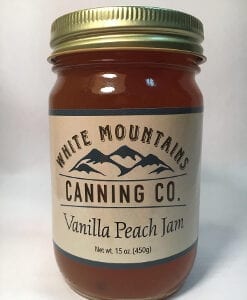 A jar of vanilla peach jam on top of a table.