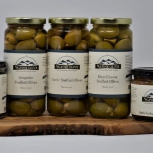 A wooden board holding jars of olives and other food.