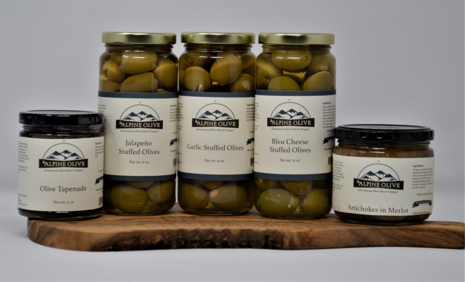 A wooden board holding jars of olives and other food.