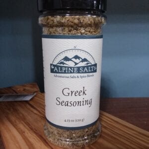 A jar of greek seasoning on top of a wooden table.
