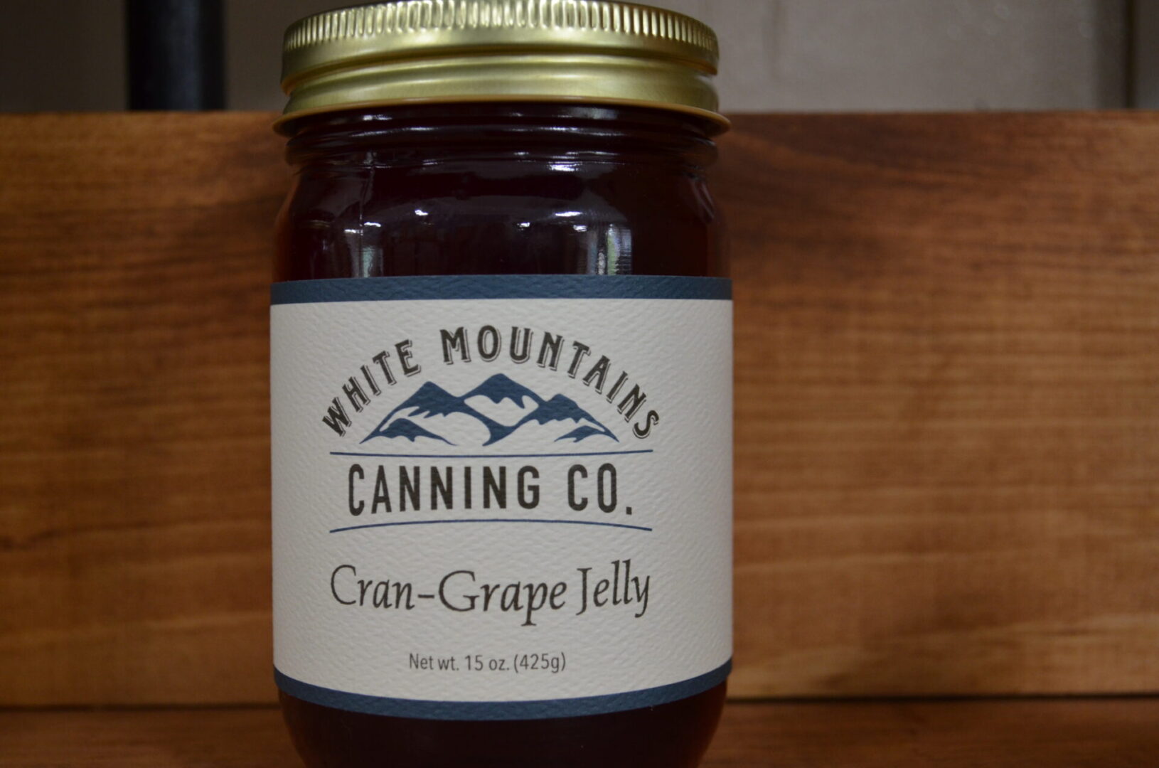 A jar of cran-grape jelly on top of a wooden table.