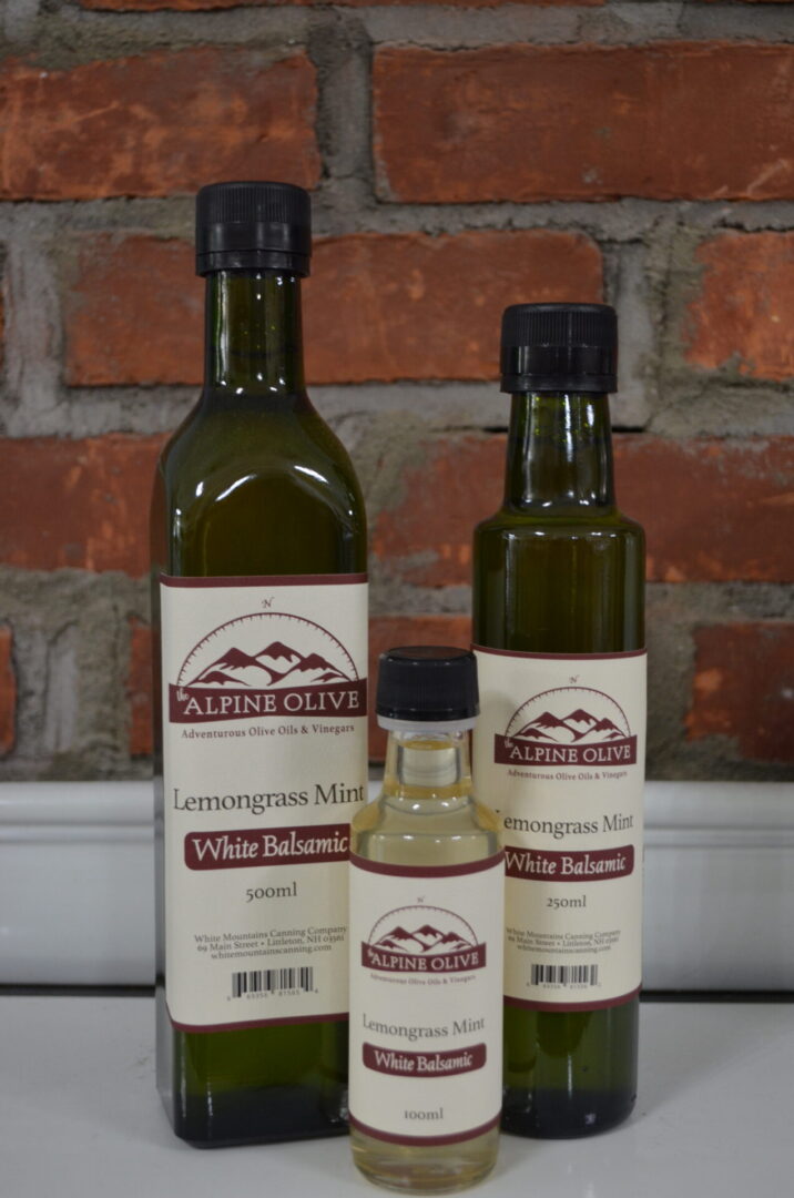 Three bottles of white balsamic vinegar on a brick wall.