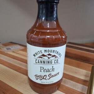 Peach BBQ sauce bottle on wooden table.